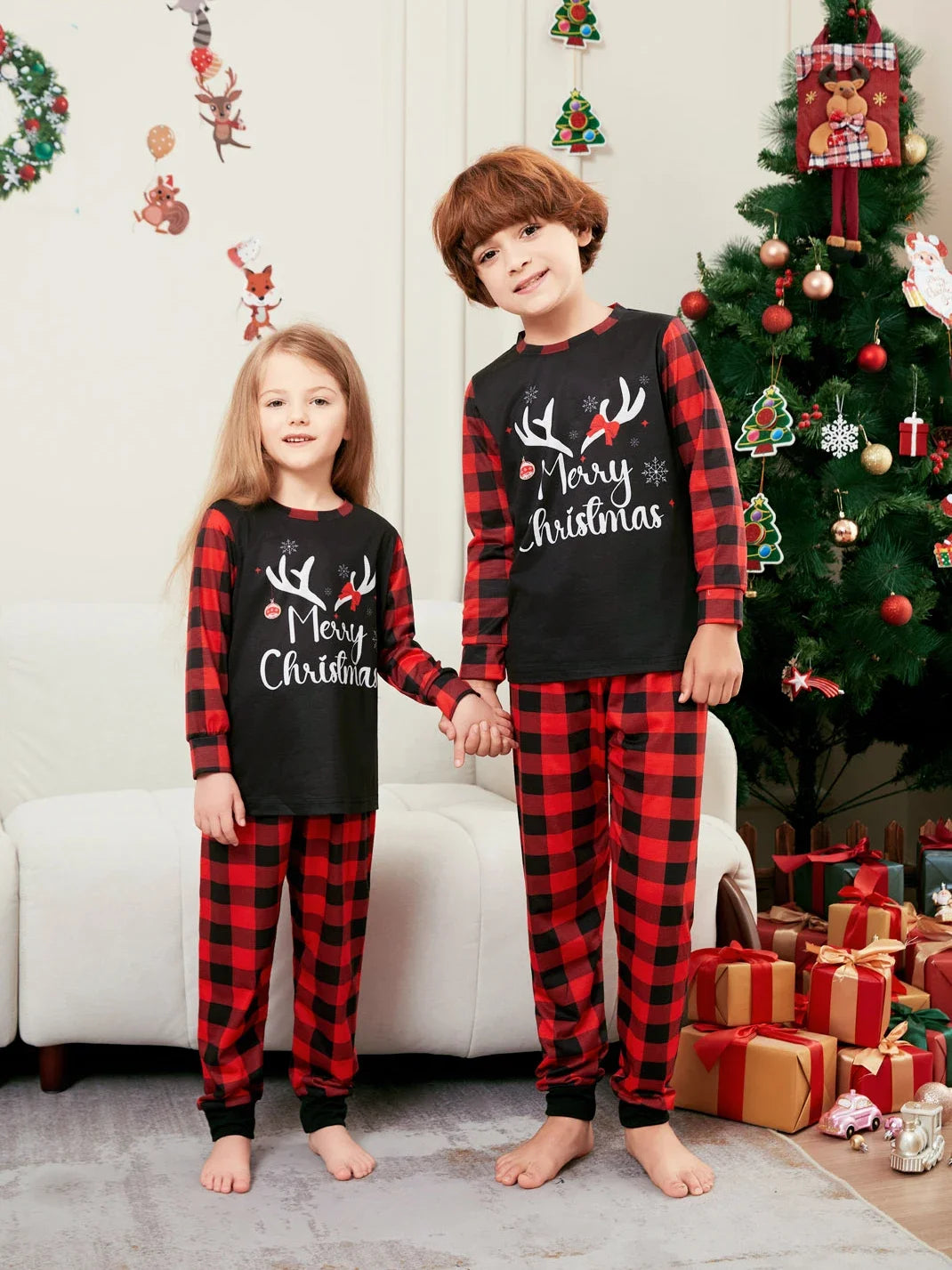 Deux enfants en pyjamas de Noël noirs à bois de renne, avec manches et pantalons à carreaux rouges et noirs.