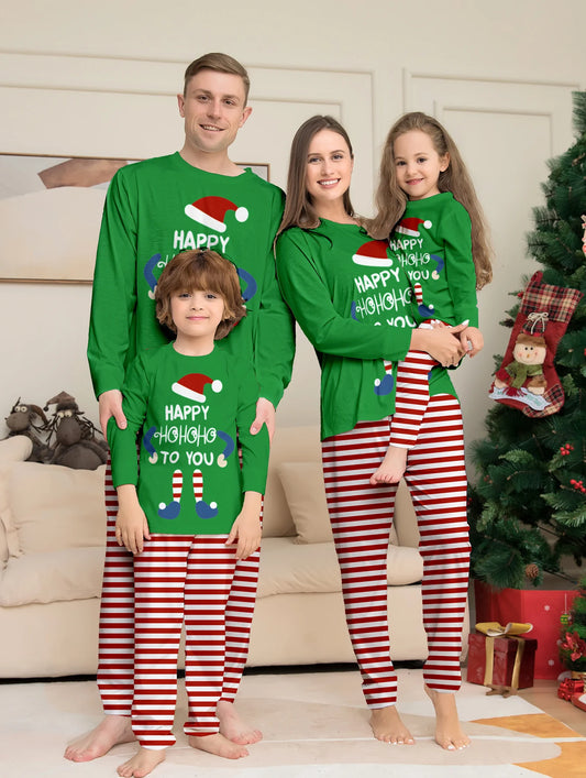 Famille en pyjamas de Noël assortis, hauts verts à motif lutin et pantalons rayés rouges et blancs, devant le sapin.